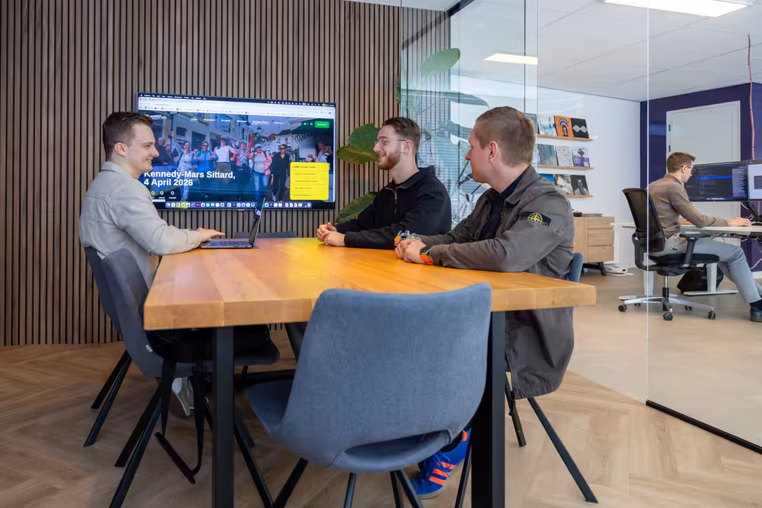 Drie personen in overlegruimte voor scherm met website