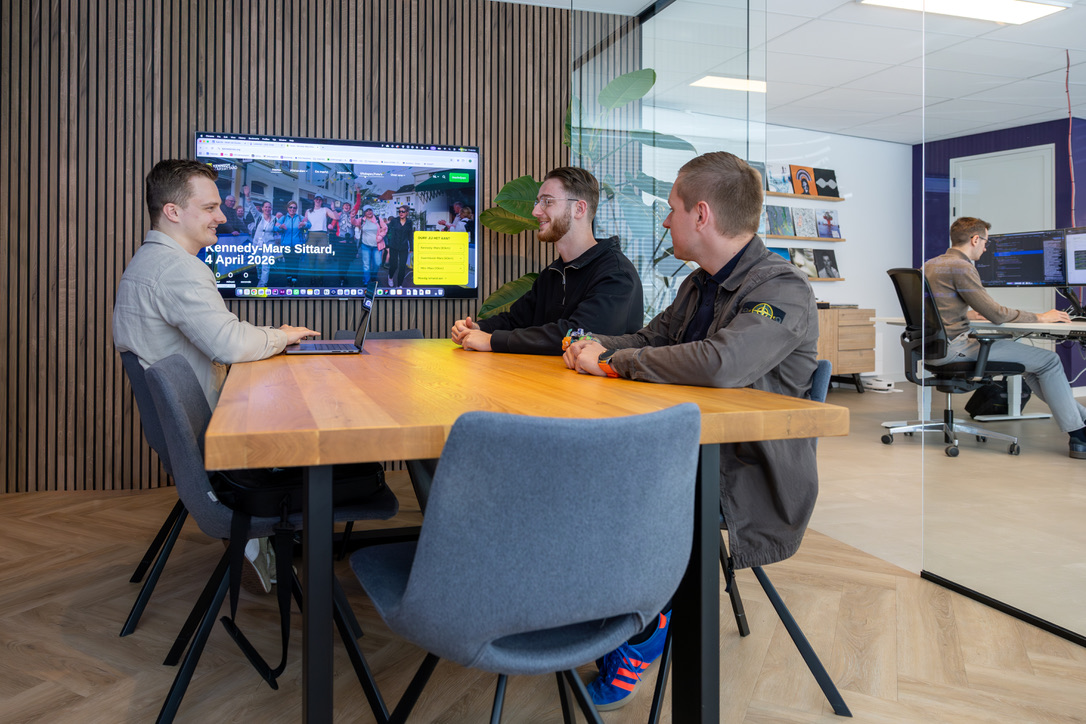 Drie personen in overlegruimte voor scherm met website